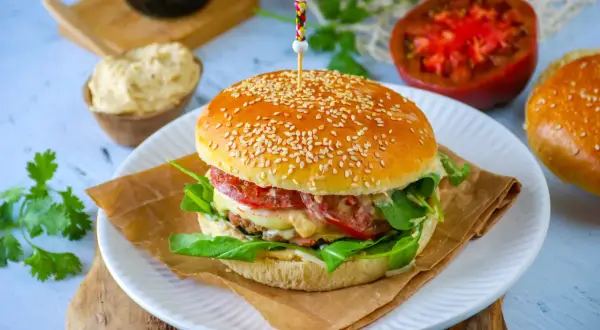 Un burger maison avec un pain aux graines de sésame, garni de légumes frais et de fromage fondant.