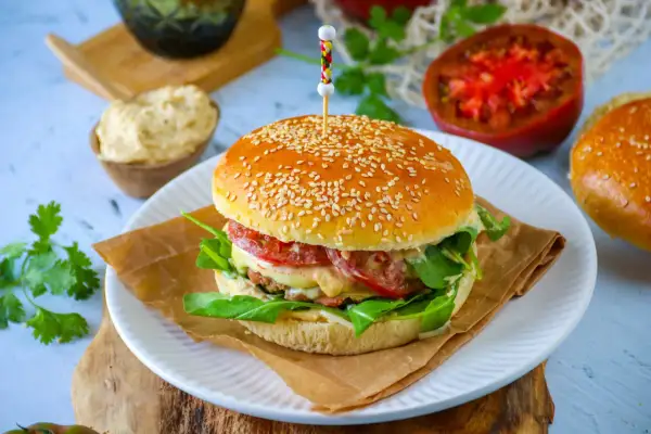 Un burger maison avec un pain aux graines de sésame, garni de légumes frais et de fromage fondant.